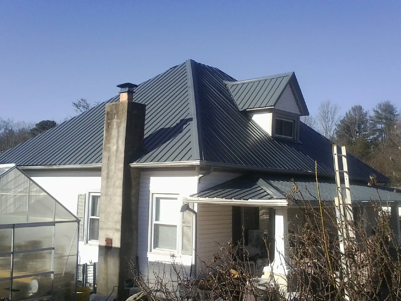 Dark blue standing seam metal roof on a white farmhouse with dormer — Slate & Tile Roof Repair by Roofing Brothers in Prospect Hill