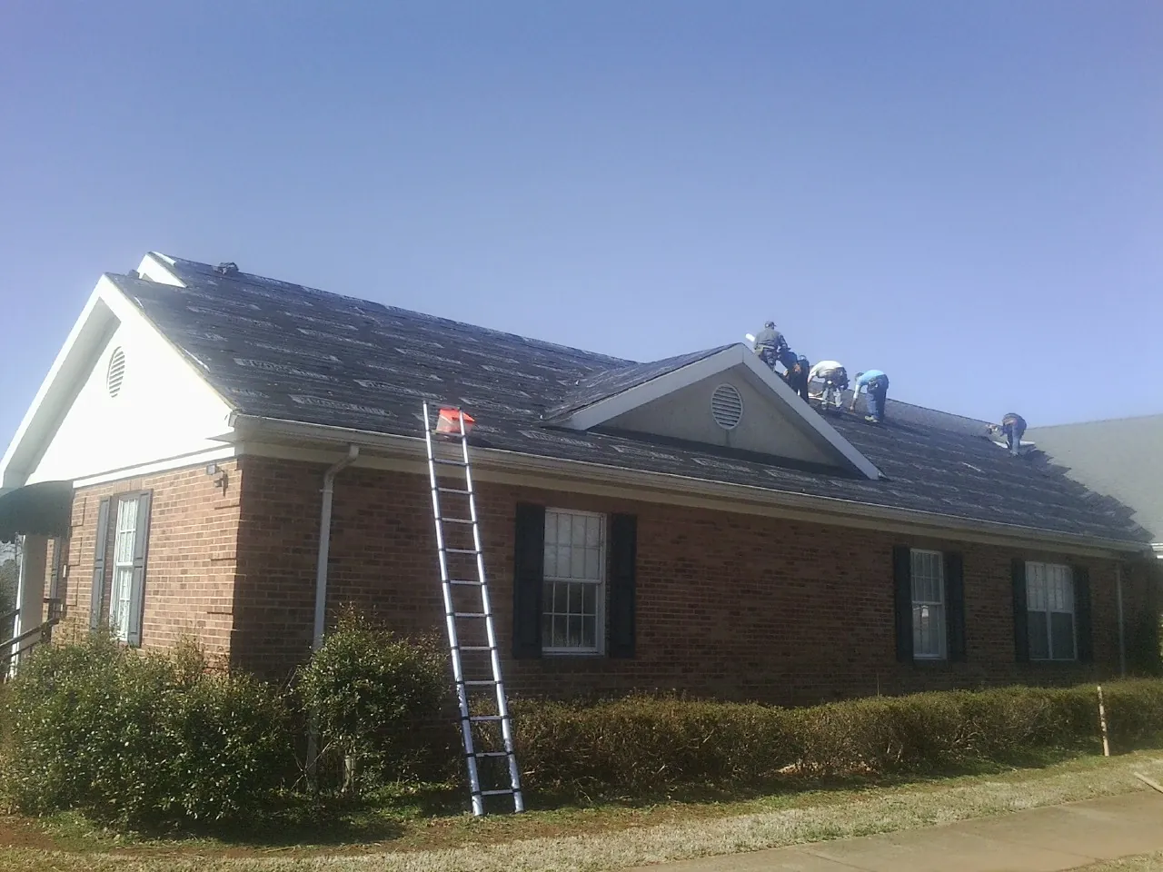 Crew tearing shingles off a brick ranch roof with a ladder set — Emergency Roof Repair work by our crew in Prospect Hill