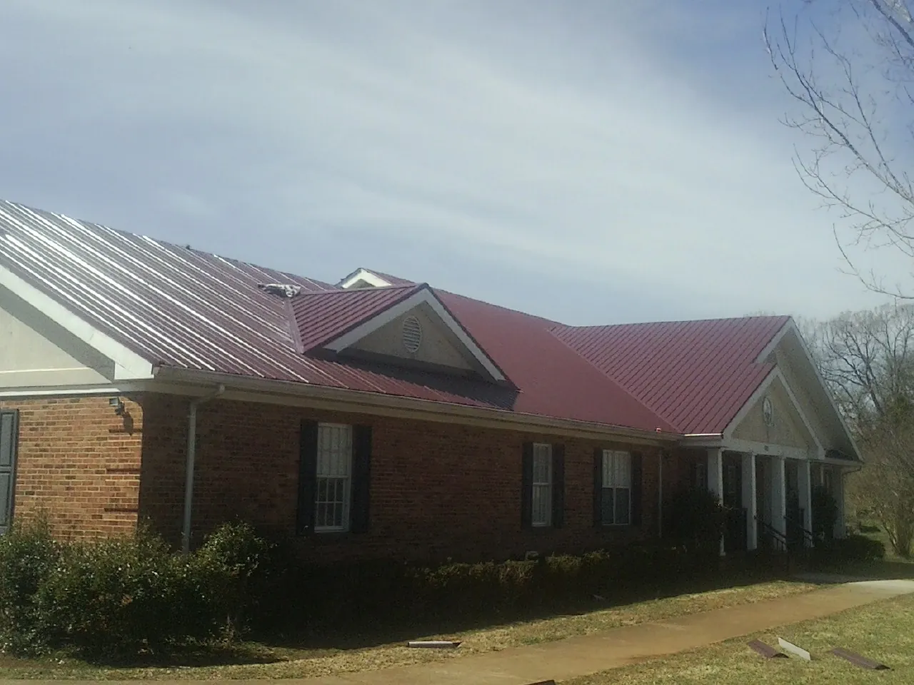 Red metal roof with gabled entries on a long brick building, from a Hail Damage Roof Repair job in Prospect Hill