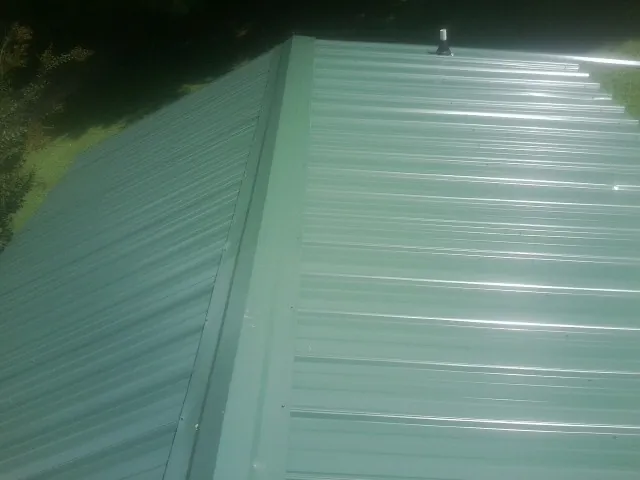 New green metal panels meeting at the ridge of a roof — Flat Roof Repair work by our crew in Prospect Hill