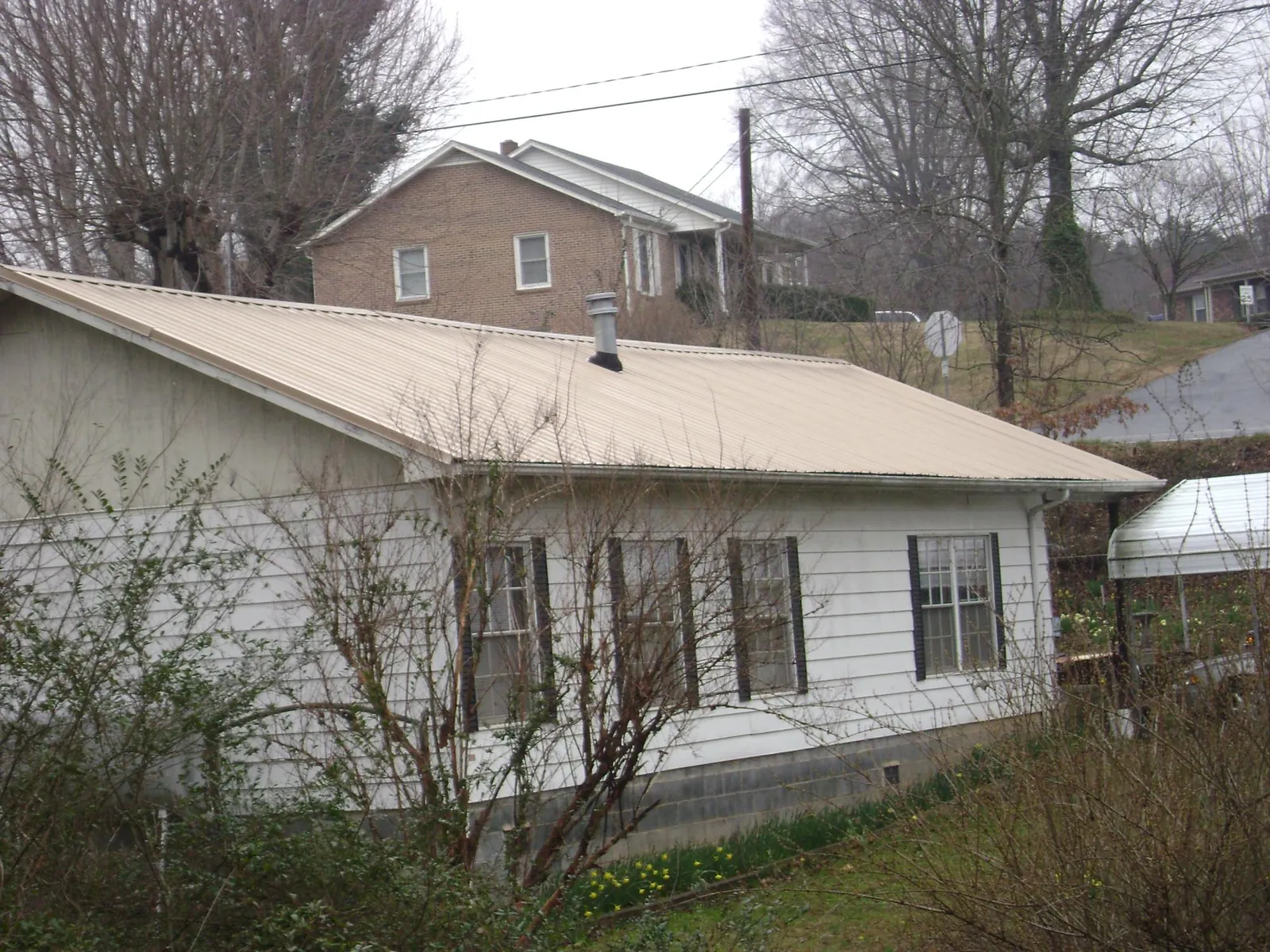 Tan metal roof on a white sided house set into a hillside — Commercial Roofing by Roofing Brothers in Prospect Hill
